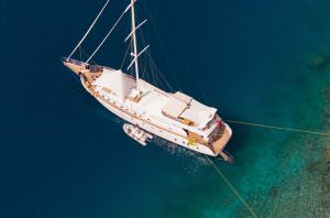 Belgin Sultan motor sailor aerial view anchored in turquoise water with tender boat, luxury yacht charter experience