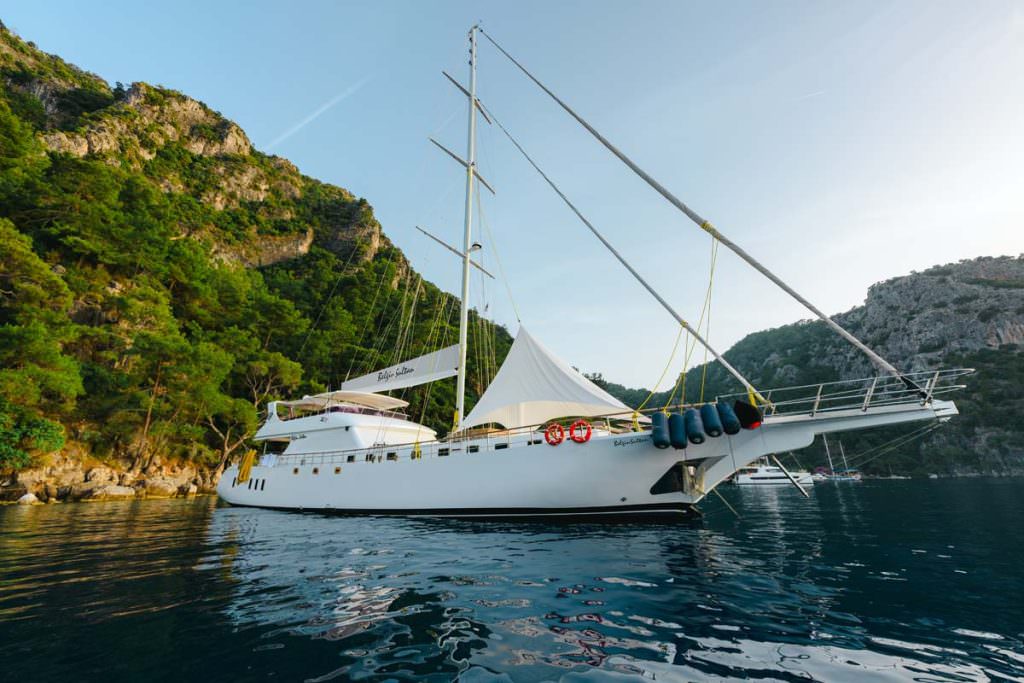 Belgin Sultan motor sailor anchored in scenic coastal bay with mountains and clear water, luxury yacht charter experience