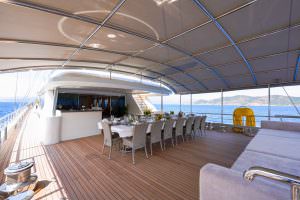 King of the Sea motor sailer aft deck lounge area, luxury yacht outdoor space with dining table, bar and comfortable seating under shaded canopy
