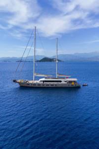 King of the Sea motor sailer exterior aerial view, luxury yacht cruising in deep blue Mediterranean waters with twin masts and elegant design