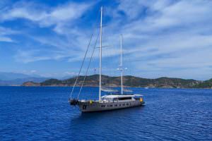 King of the Sea yacht charter motor sailer exterior profile view, luxury yacht sailing in crystal clear Mediterranean waters with elegant twin mast design