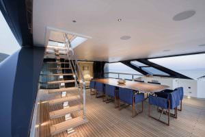 Legasea luxury yacht upper deck dining area with wooden table, blue chairs and staircase access