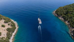 North Wind motor sailer aerial view, luxury yacht cruising through turquoise waters between islands, exclusive yacht charter experience and Mediterranean scenery