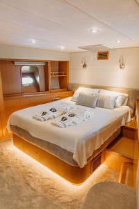 Reis yacht master cabin with soft ambient lighting, double bed and elegant wooden interior, luxury yacht charter experience